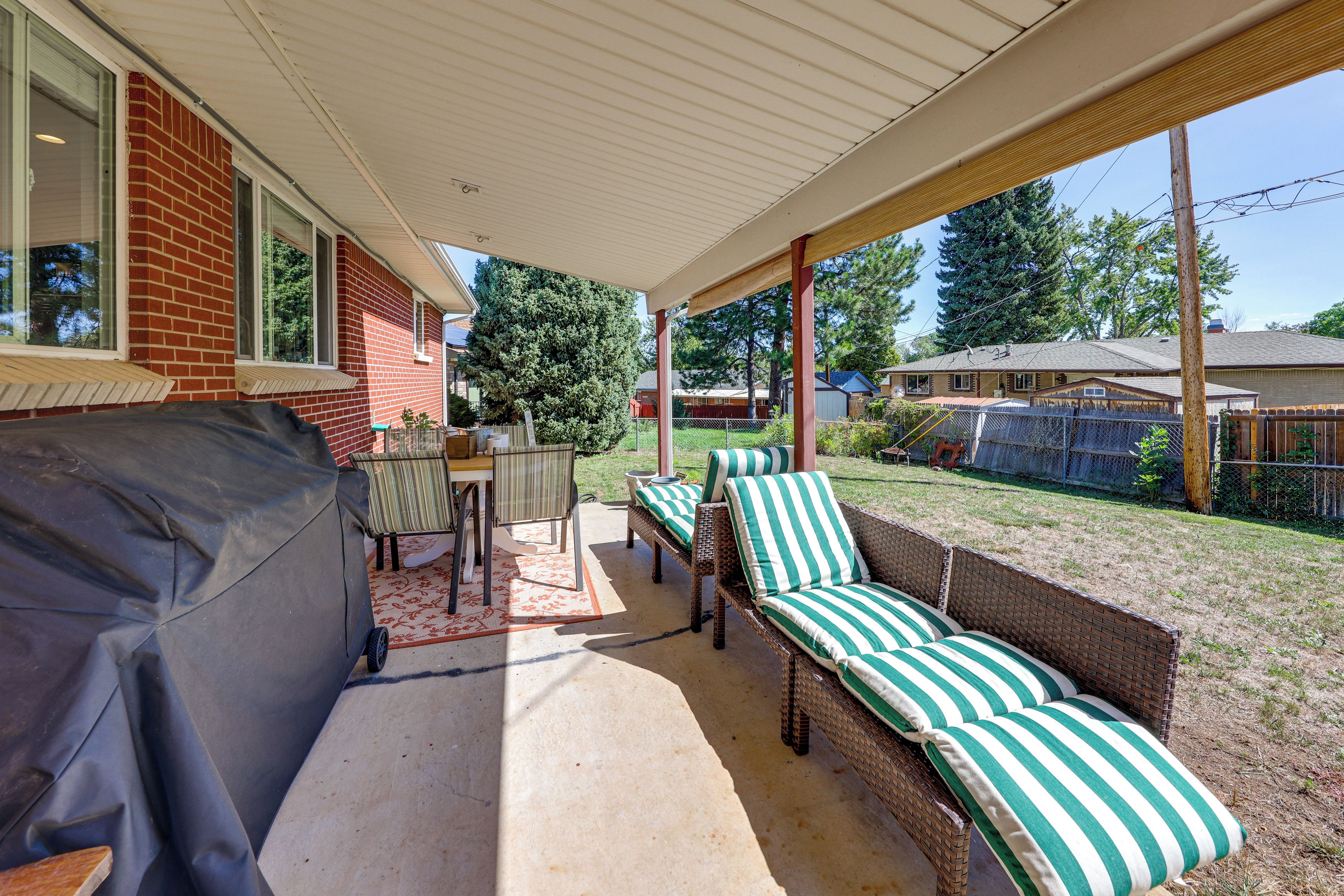 A covered patio with a barbecue, outdoor furniture, and a view of the backyard.
