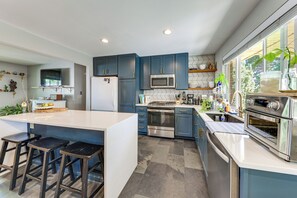 Cozinha moderna com ilha central, banquetas, eletrodomésticos de aço inoxidável e janela com vista.