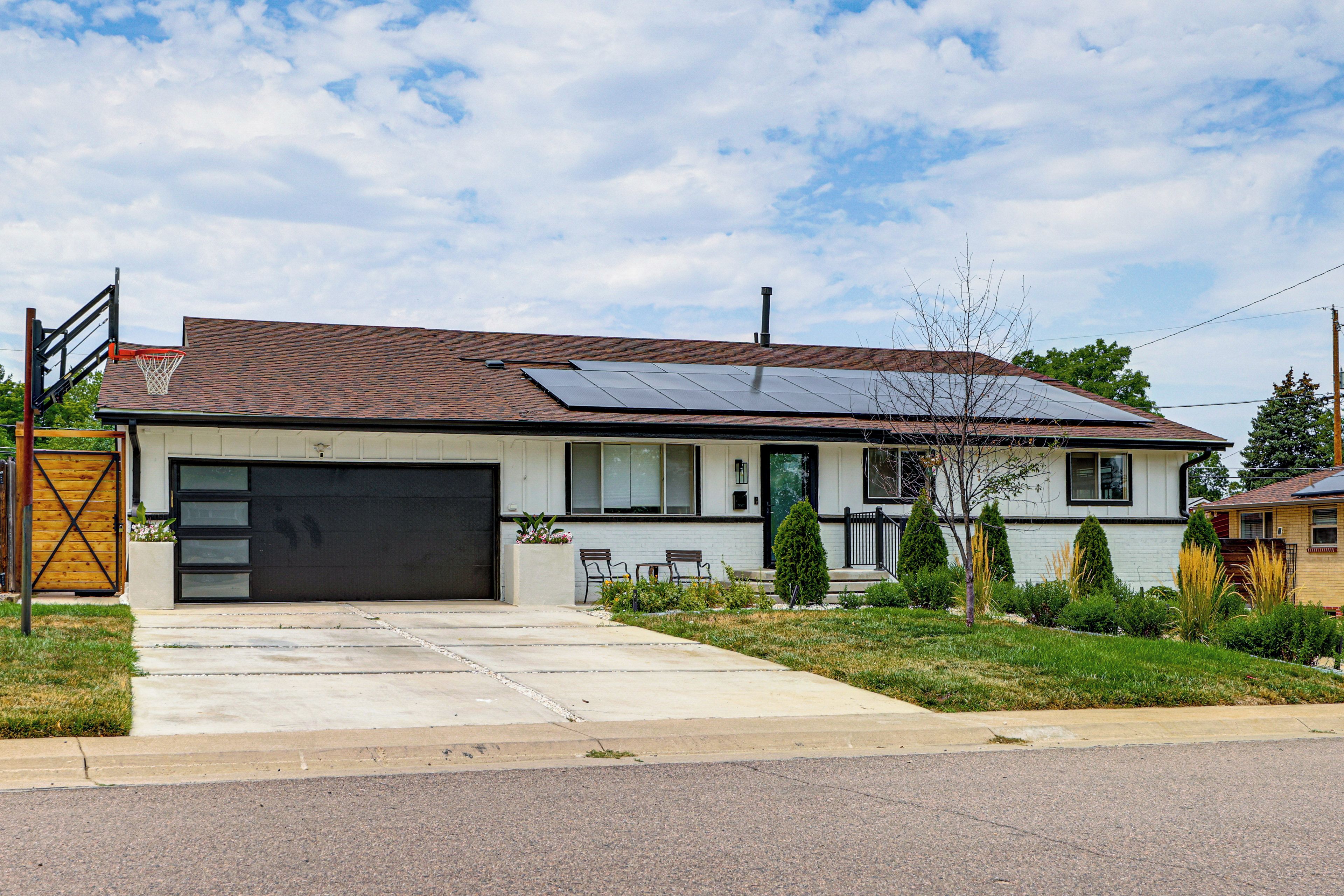 A residential house with a garage, solar panels, a front porch with seating, and a well-maintained lawn.