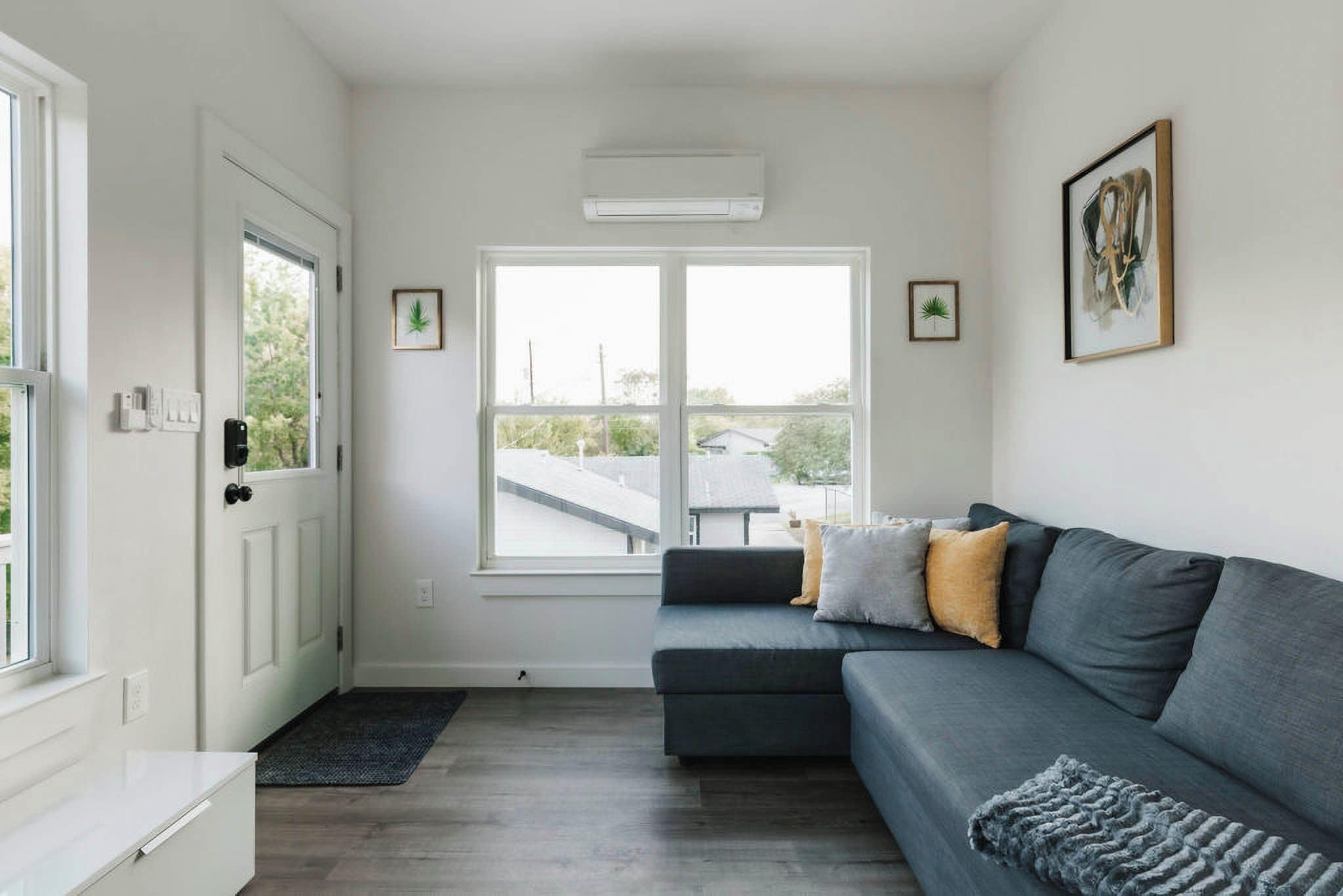 Ein modernes Wohnzimmer mit einem grauen Sofa, einem kleinen Fenster und einer Tür.