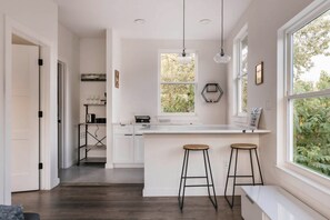 A modern kitchen with a central island, bar stools, pendant lights, and a window with a view of greenery. - East Austin Tiny Home - 4 Mi to Dtwn! (Austin)