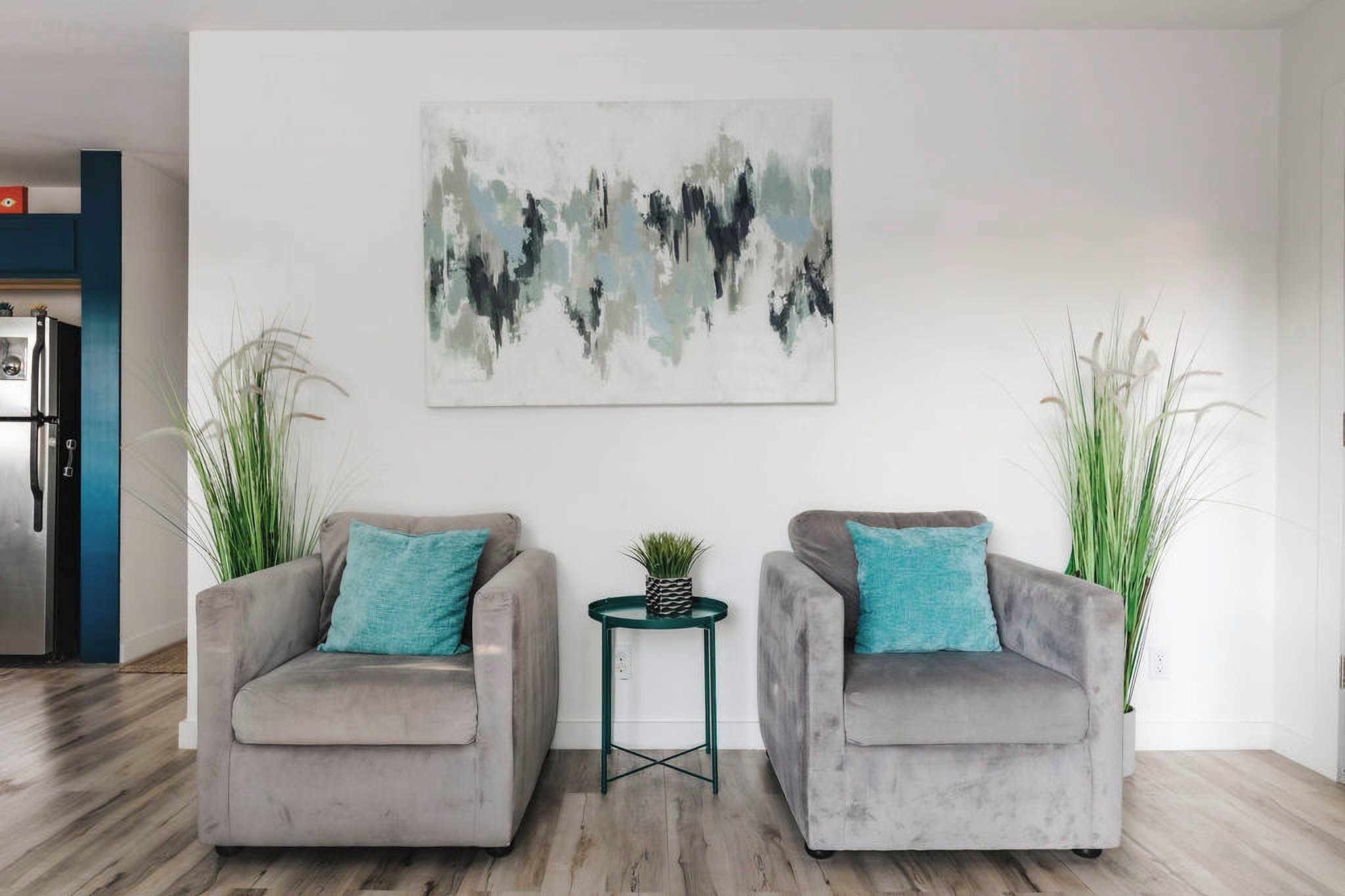 Ein modernes Wohnzimmer mit zwei grauen Sesseln, einem kleinen runden Tisch mit einer Pflanze und abstrakter Kunst an der Wand.