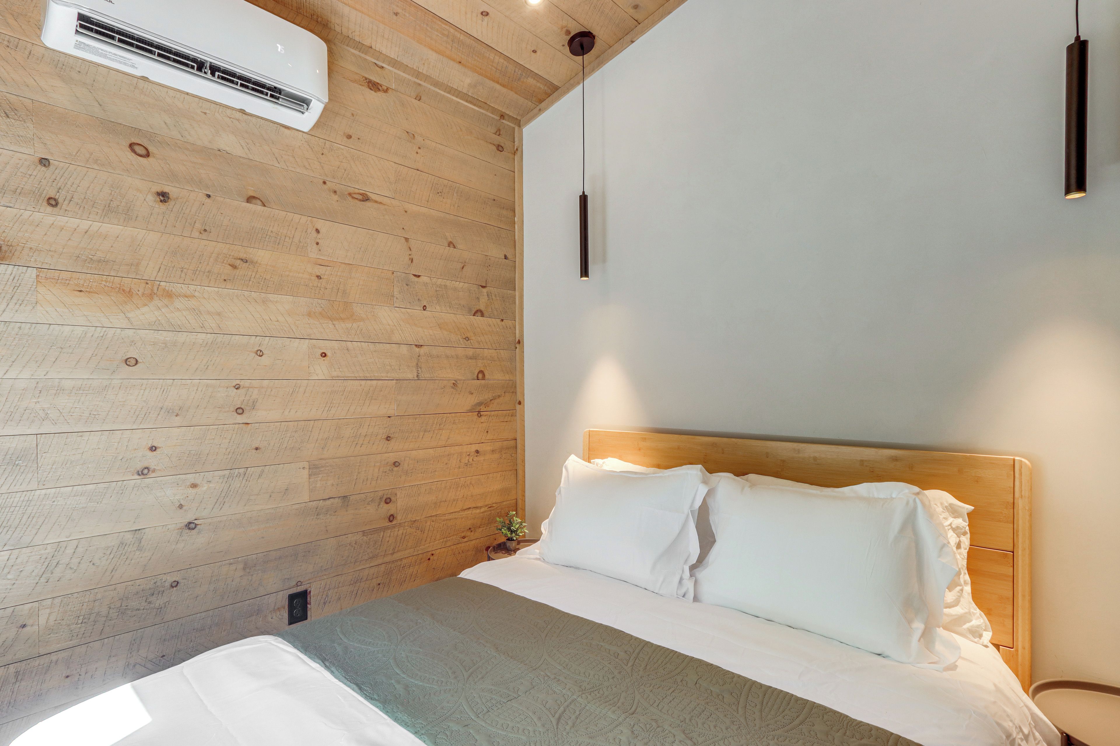 Een slaapkamer met een wand van houten latten, een bed met witte beddengoed en een hanglamp.