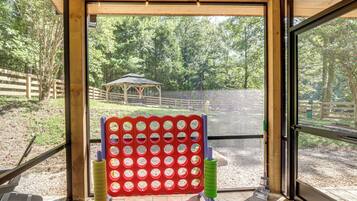 A room with a large window, a wooden ceiling, and a view of an outdoor area with a fenced enclosure and a small structure.