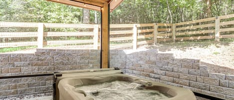 A hot tub under a wooden pergola with a brick wall backdrop and a wooden fence in the background.