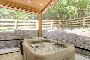 Una vasca idromassaggio sotto un gazebo in legno, con un muro di mattoni sullo sfondo e una recinzione in legno in lontananza.