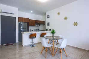 A modern kitchen with a refrigerator, microwave, and coffee maker. There is a dining area with a glass table and white chairs. - 3 Mi to Beach! Condo w/ Pool in Puerto Morelos (Puerto Morelos)