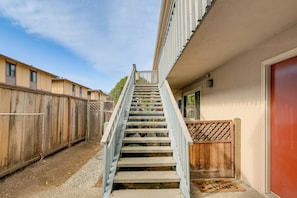 Escadaria de concreto que leva a um edifício, com cerca de madeira de um lado e porta vermelha do outro.