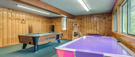 Una sala con billar, paredes de madera, mesa de billar y mesa de futbolín.