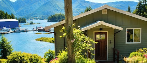 A cabin with a wooden deck, a door, and a view of a lake and mountains.