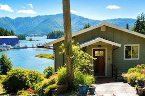 A cabin with a wooden deck, a door, and a view of a lake and mountains.