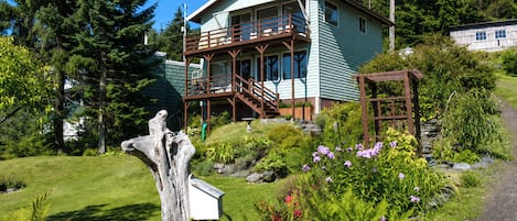 A two-story house with a balcony, surrounded by lush greenery and a clear sky.