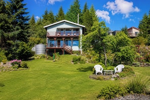 A two-story house with a balcony, surrounded by a well-maintained garden and trees.