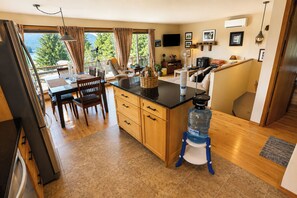 A modern kitchen with a large water dispenser, wooden cabinets, and a dining area with a view of greenery.