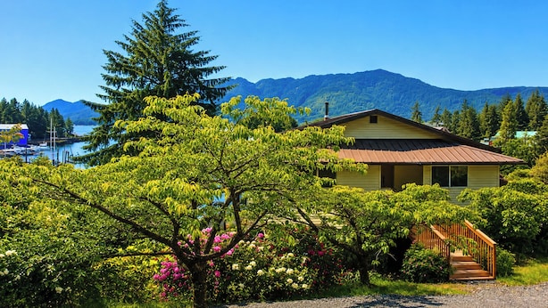 Una casa con una scala in legno che conduce a un portico, circondata da vegetazione rigogliosa e con le montagne sullo sfondo.