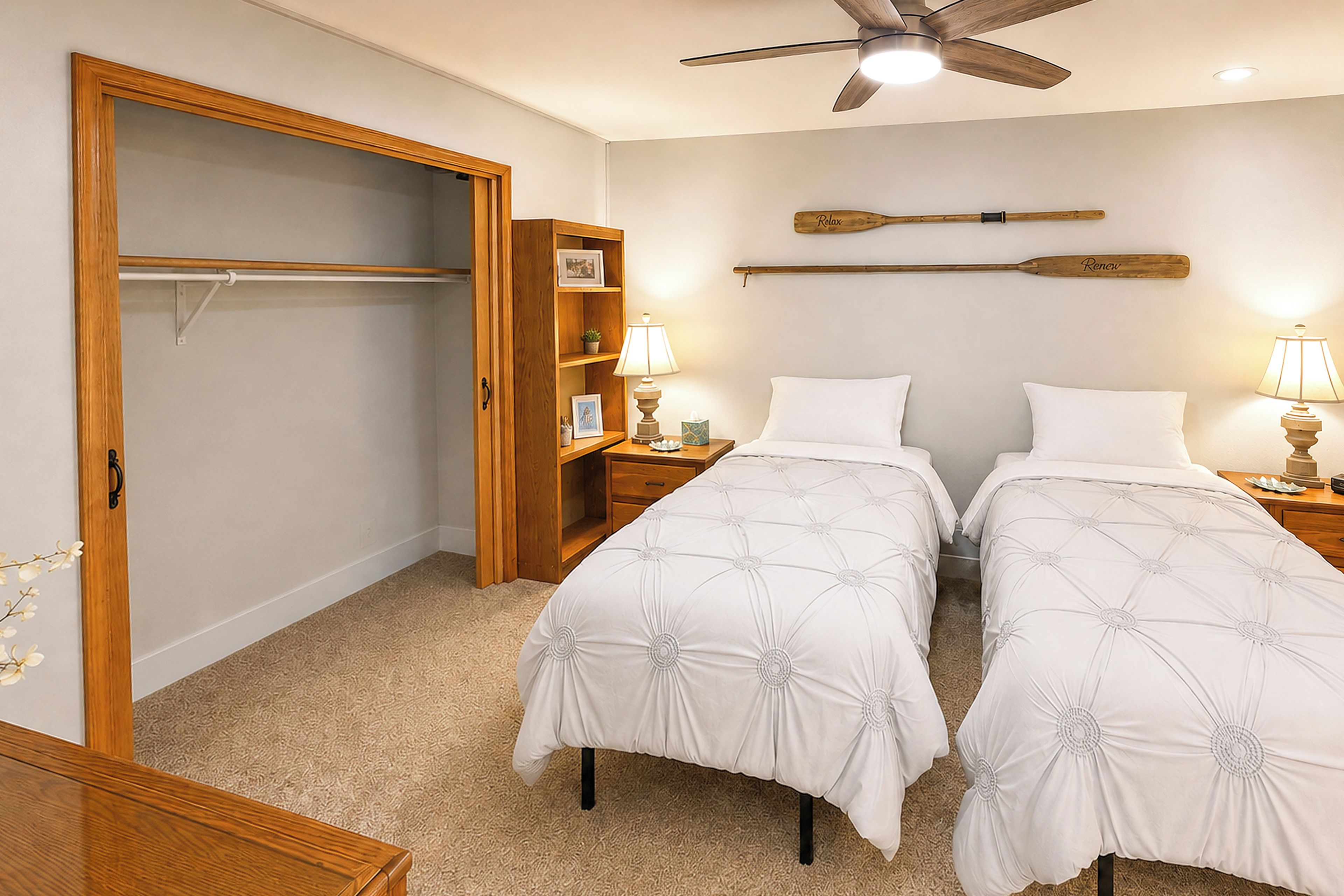 A bedroom with two beds, a wooden wardrobe, a ceiling fan, and a wall-mounted shelf with decorative items.
