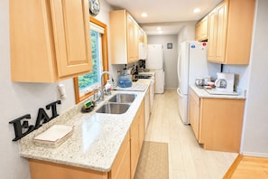 A kitchen with wooden cabinets, a granite countertop, a sink, and a refrigerator. - Ketchikan Beach Retreat Dock On-site (Ketchikan)