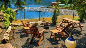 Zona salotto all'aperto sul lago, con sedie e tavoli di legno, un barbecue e vista sul lago e sulle montagne.