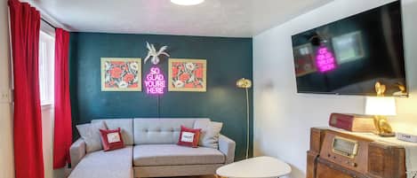 A living room with a sectional sofa, a small table, a vintage radio, and a TV mounted on the wall.