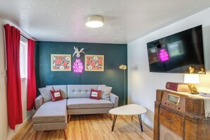 Una sala de estar con un sofá modular, una mesita, una radio antigua y un televisor montado en la pared.