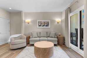 Una sala de estar moderna con un sofá gris, un sillón estampado, una mesa redonda de centro y dos lámparas fijadas a la pared.