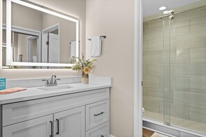 A bathroom with a white vanity, a mirror, a sink, a towel rack, and a shower with glass doors. - Salt Life Retreat - Waterfront Getaway in the Heart of Morehead City! (Morehead City)