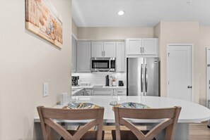 A modern kitchen with white cabinets, stainless steel appliances, and a dining area with a white table and wooden chairs. - Salt Life Retreat - Waterfront Getaway in the Heart of Morehead City! (Morehead City)