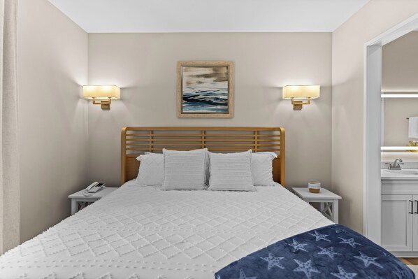 A hotel room with a bed, bedside tables, a phone, wall-mounted lamps, and a painting. - Salt Life Retreat - Waterfront Getaway in the Heart of Morehead City! (Morehead City)