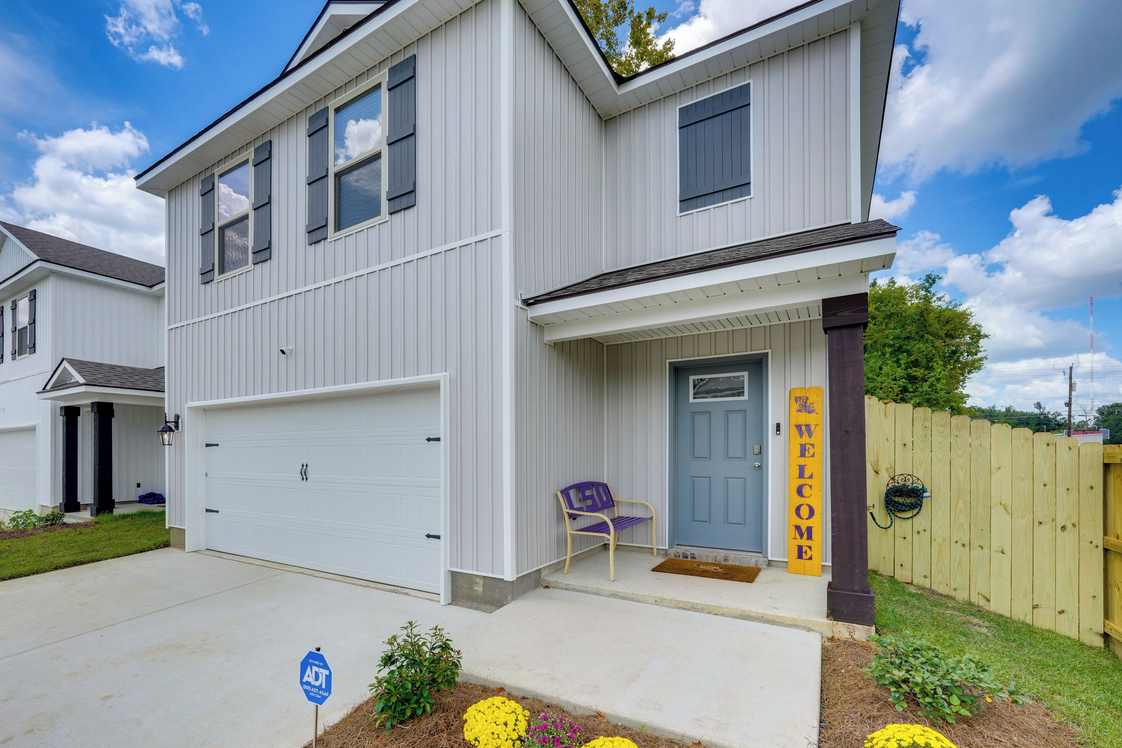 A two-story residential building with a garage, a front porch with a bench, and a welcome sign.