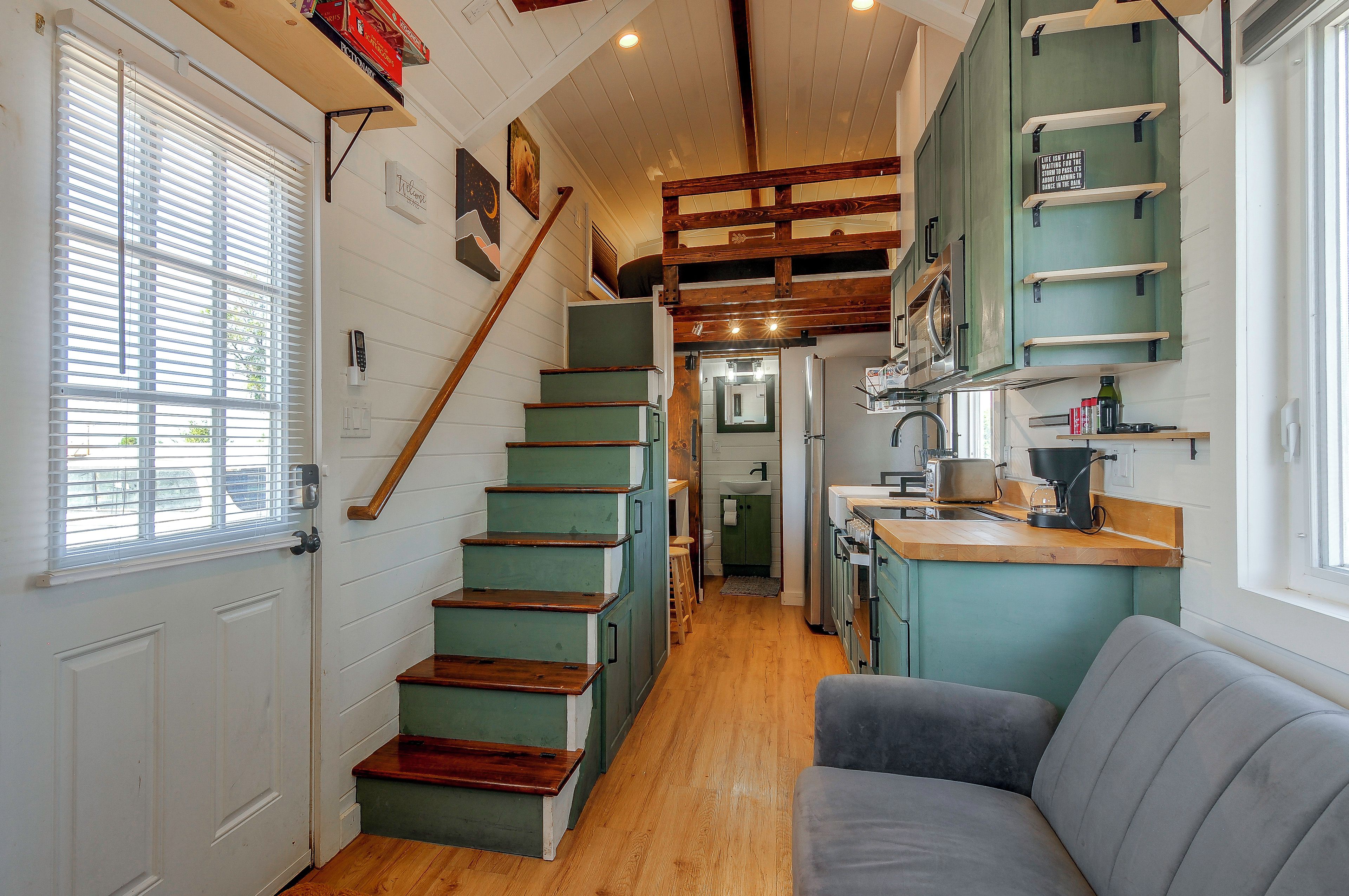 A staircase with wooden steps leading to a loft area, a kitchen with a sink and cabinets, and a gray sofa in a cozy living space.