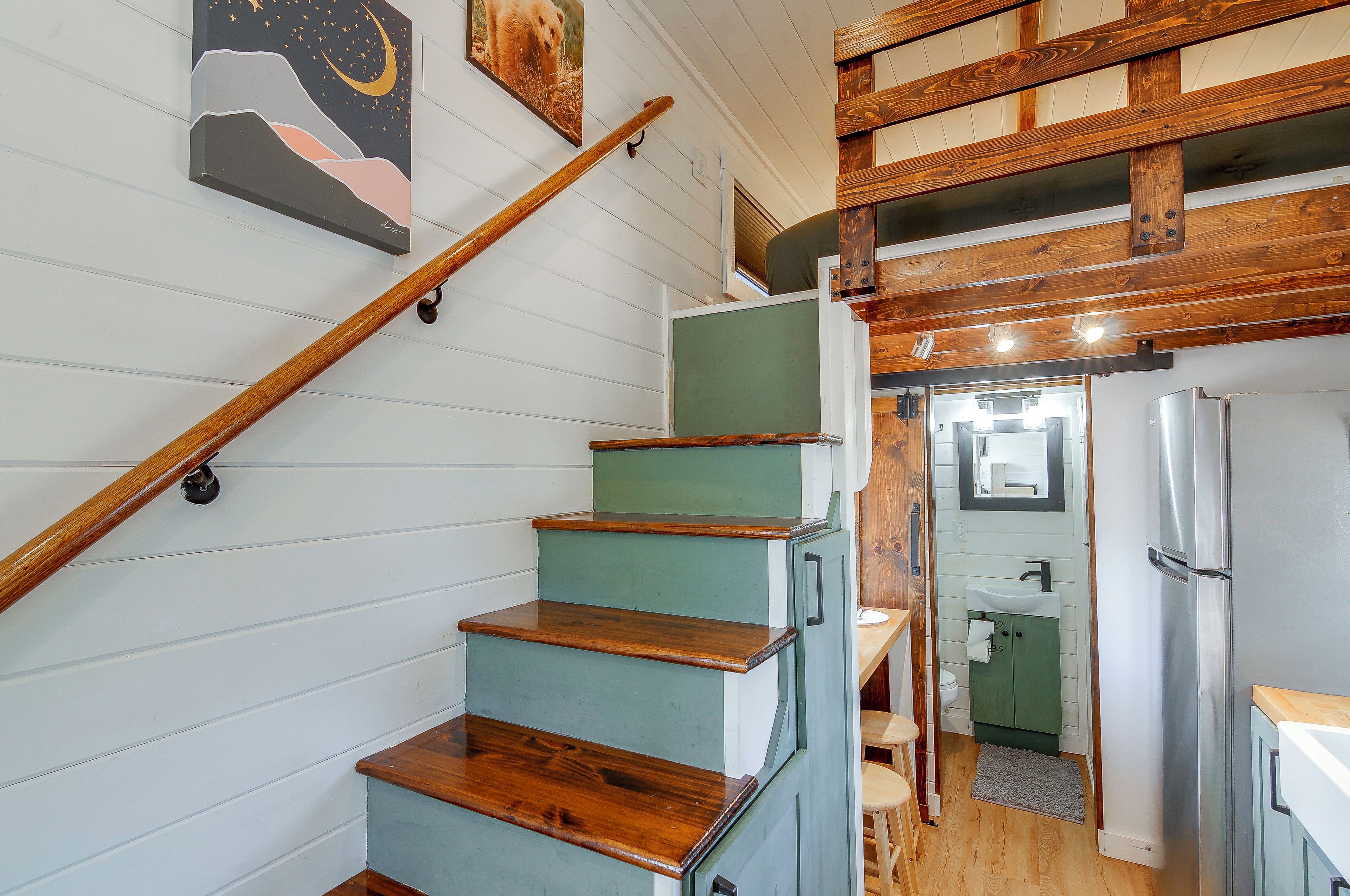 A staircase with wooden steps and a handrail, leading to a room with a green door and a white sink.