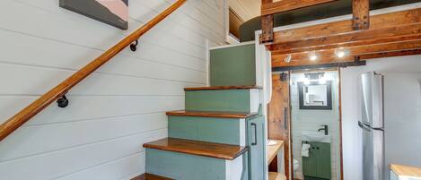 A staircase with wooden steps and a handrail, leading to a room with a green door and a white sink.