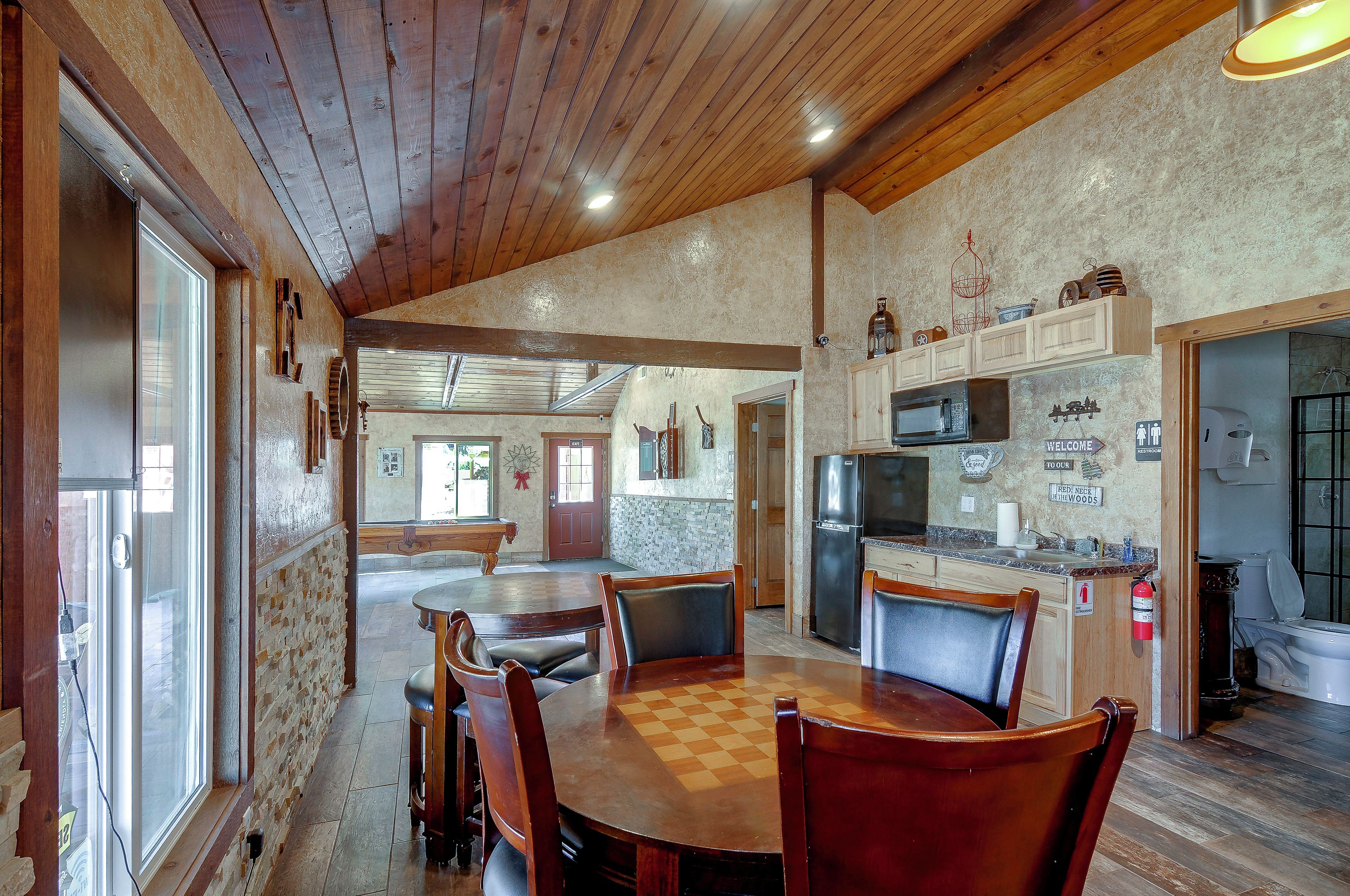 Un vaste espace de salle à manger avec une table et des chaises en bois, une cuisine équipée d’appareils modernes et une vue à travers la porte vitrée.