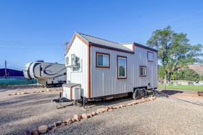 A small, single-story RV with a white exterior and brown trim, parked on a gravel surface with a clear sky in the background. - 30 Mi to Zion! Mtn-view Tiny Home Escape (Kanab)