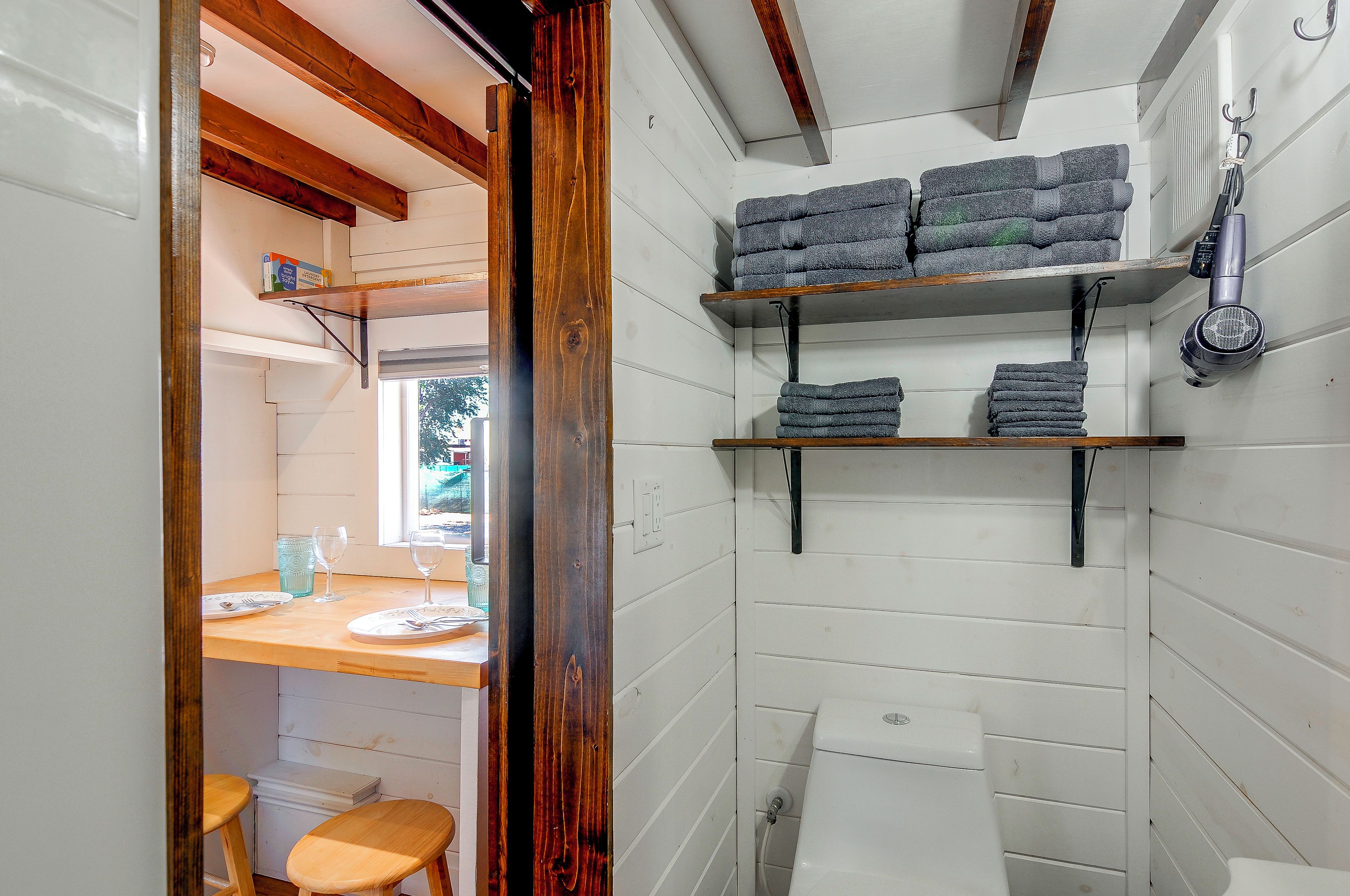 A compact bathroom with white walls, wooden beams, and shelves holding towels.