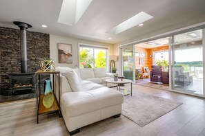 A modern living room with a fireplace, white sofa, and a glass door leading to an outdoor area. - Waterfront Whidbey Island Oasis! Hot Tub + Patio (Freeland)
