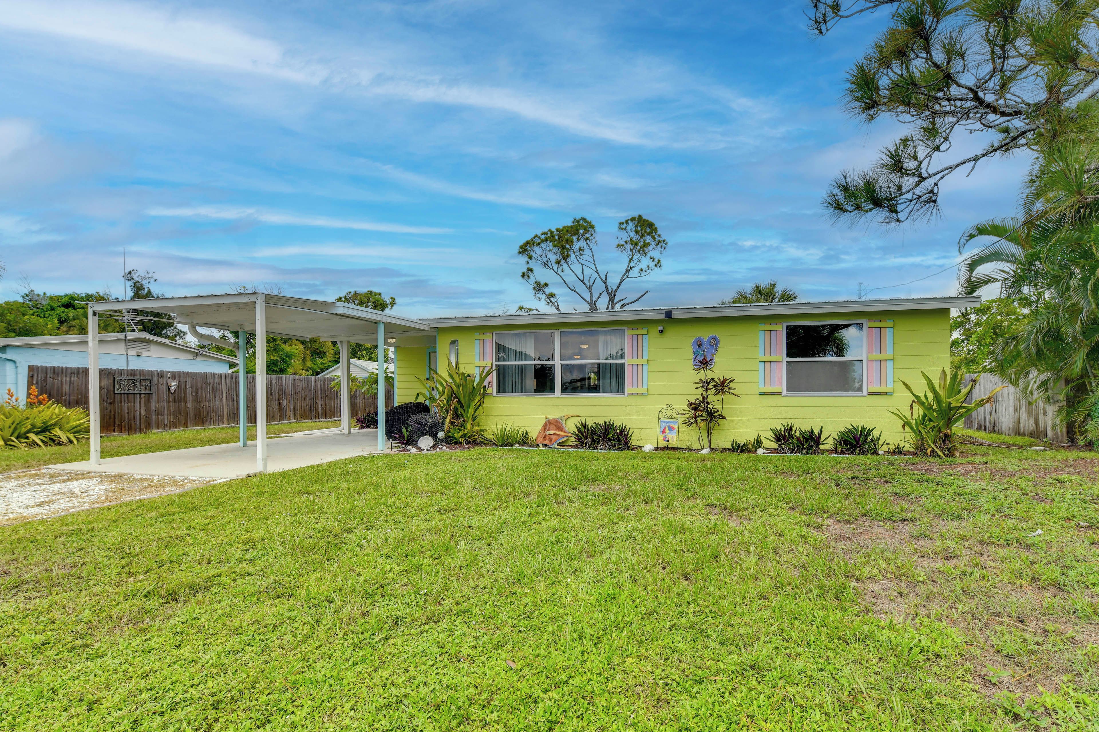 A single-story house with a covered patio area, a fenced yard, and a variety of plants.