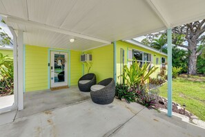 A covered porch with a concrete floor, two wicker chairs, and a door with a 'Welcome' sign. - Canal-front Englewood Cottage Near Beaches (Englewood)