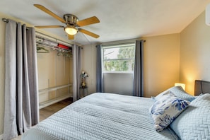 Ein Schlafzimmer mit Bett, Deckenventilator, Fenster und Kleiderschrank mit Kleidung.