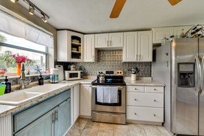 Eine Küche mit weißen Schränken, einem Edelstahlkühlschrank, einer Mikrowelle, einem Backofen und einem Fenster mit Blick auf Palmen.