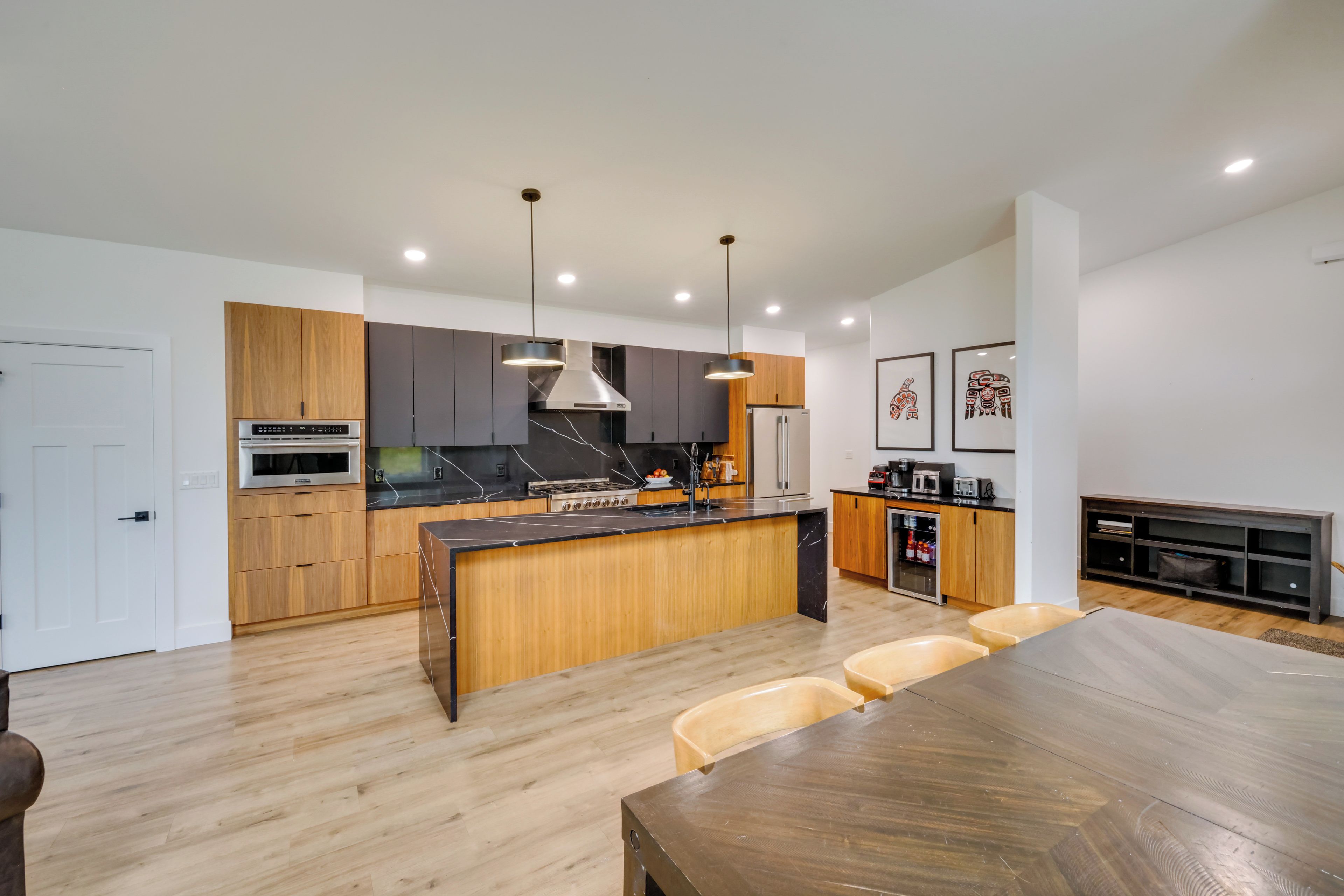 A modern kitchen with a central island, wooden cabinets, and a dining area with a large table and chairs.