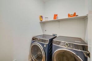 Un área de lavandería con dos lavadoras de carga frontal y un estante superior con productos de limpieza.