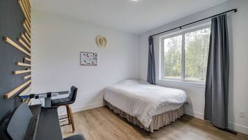 A bedroom with a bed, a desk, a chair, a window with curtains, and a wall-mounted hat.