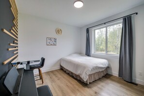 Un dormitorio con cama, escritorio, silla, ventana con cortinas y un sombrero colgado en la pared.