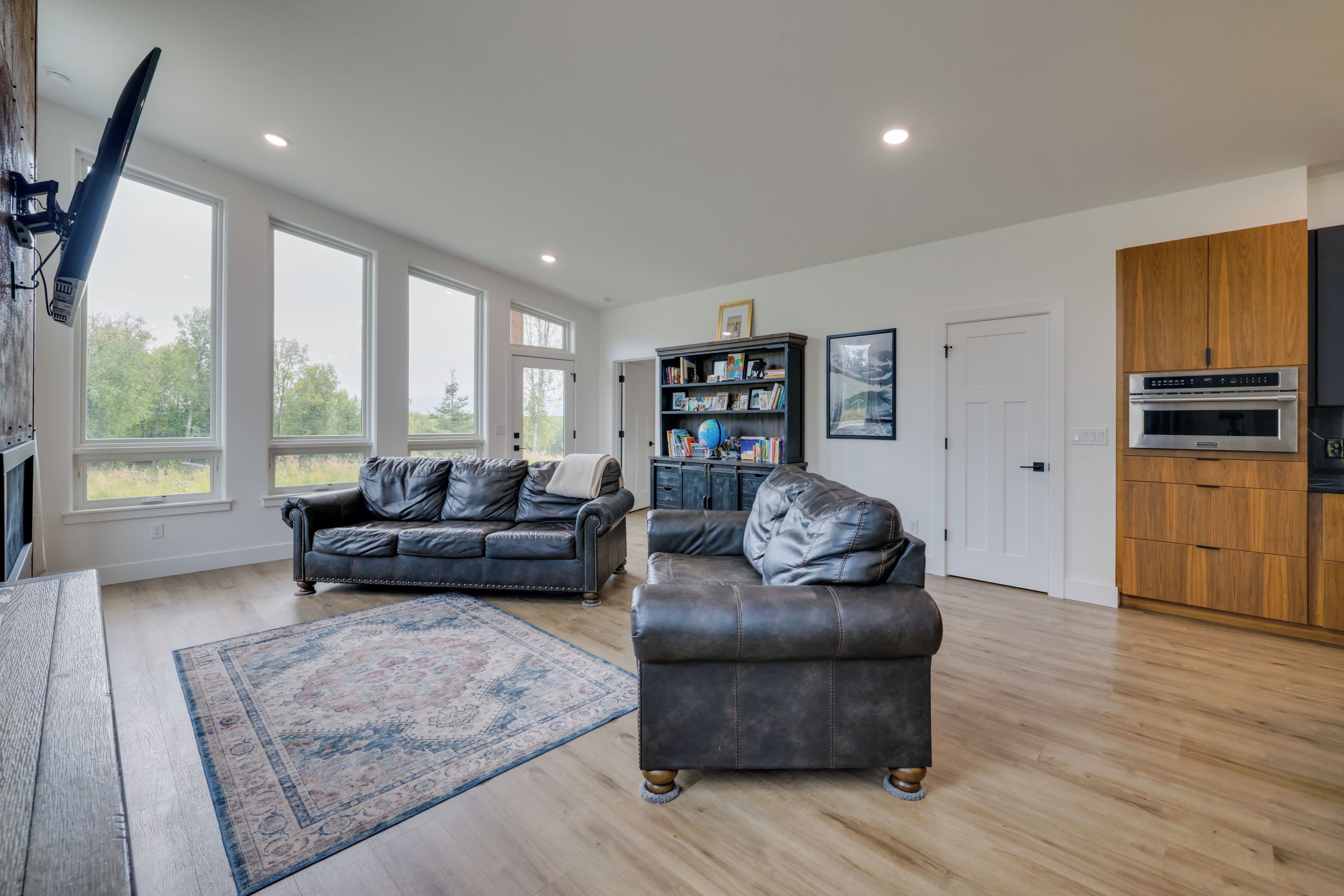 A spacious living area with a large window, a leather sofa, a coffee table, and a bookshelf.