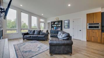 A spacious living area with a large window, a leather sofa, a coffee table, and a bookshelf.
