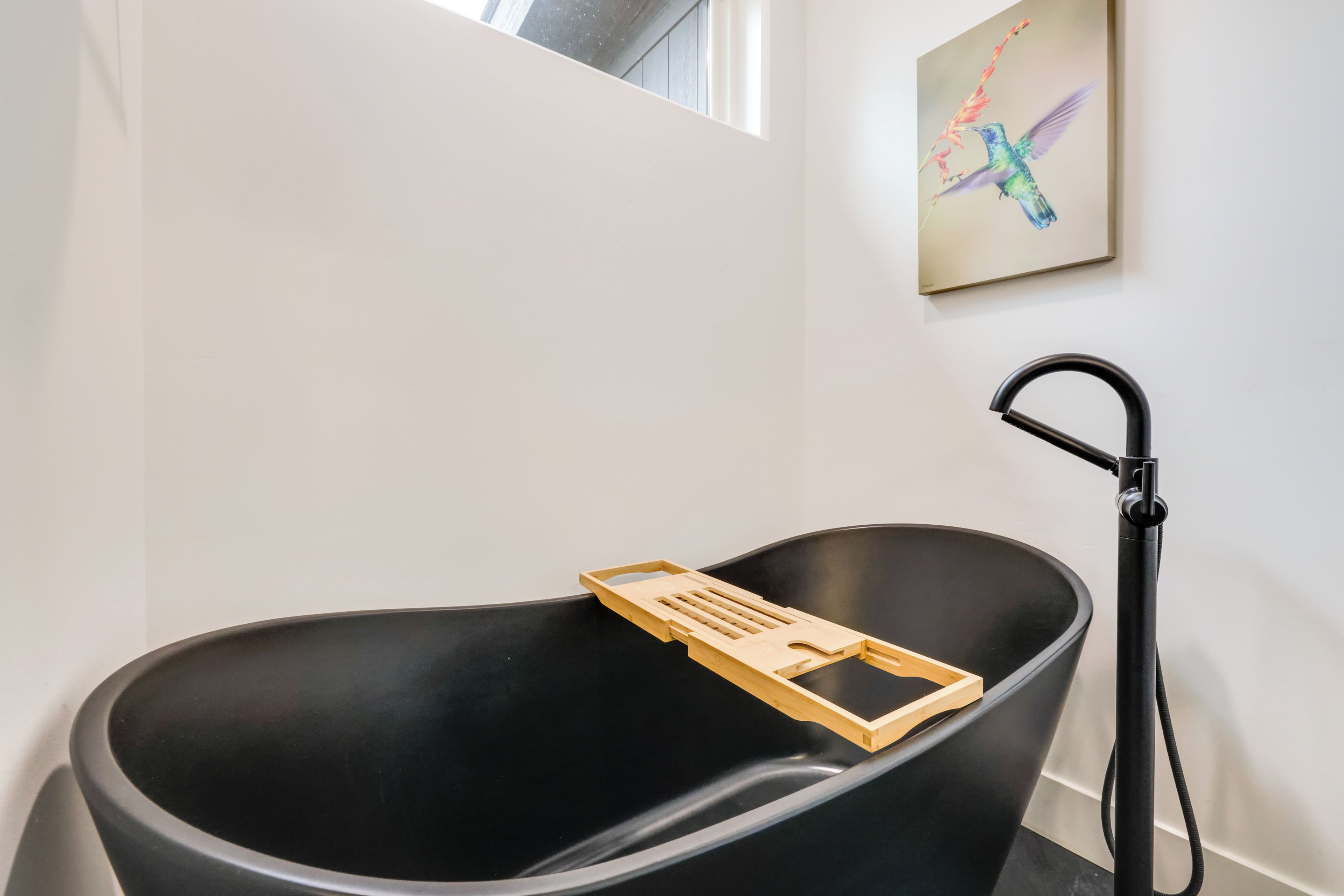 A modern bathroom with a black bathtub, a wooden tray, and a black faucet.