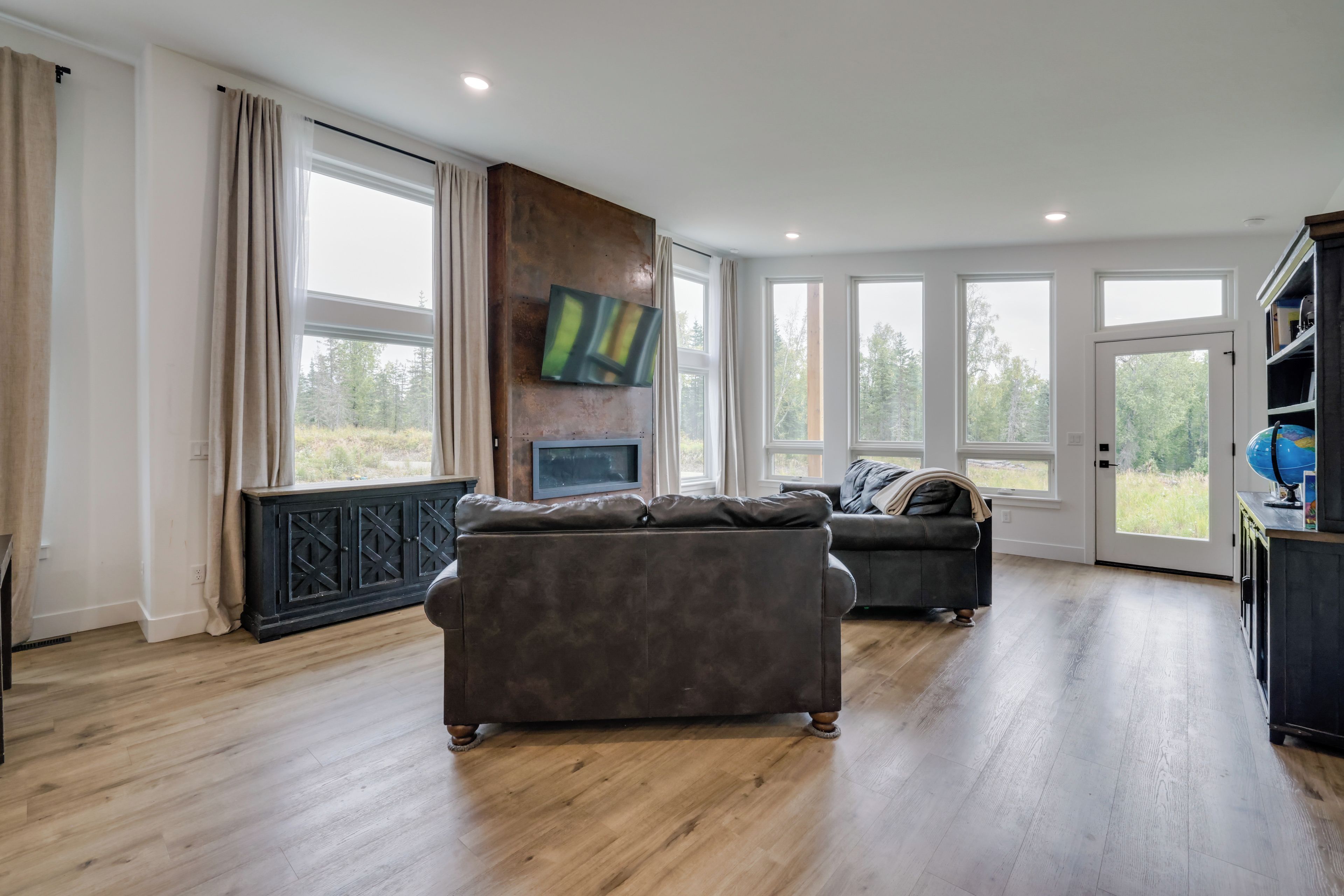A spacious living room with a fireplace, large windows, and a flat-screen TV mounted on a wooden wall.