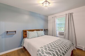 Une chambre à coucher comprenant un lit, une table de chevet, une fenêtre avec des rideaux et un luminaire fixé au mur.