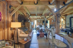 A rustic cabin interior with a wooden ceiling, a leather sofa, a dining table, and a fireplace. - Fire Pit, Deck! Rural Retreat Near East Beach (Charlestown)